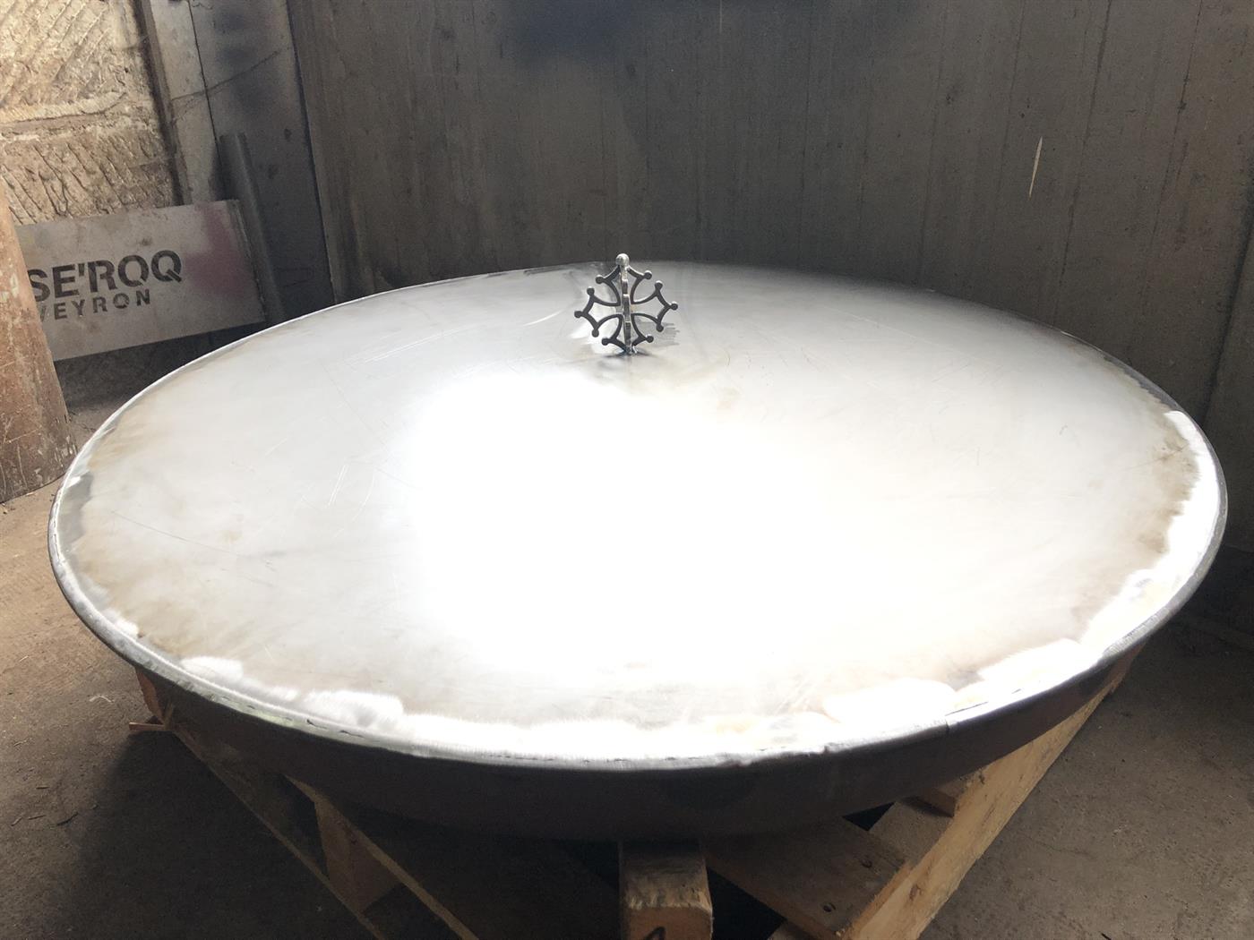 Grande cuve bombée en acier brossé posée à l'atelier, ornée d'une croix occitane