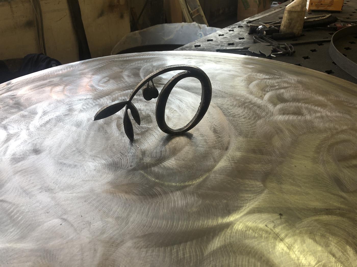 Détail d'un rameau d'olivier découpé dans l'acier, posé sur une cuve brossée